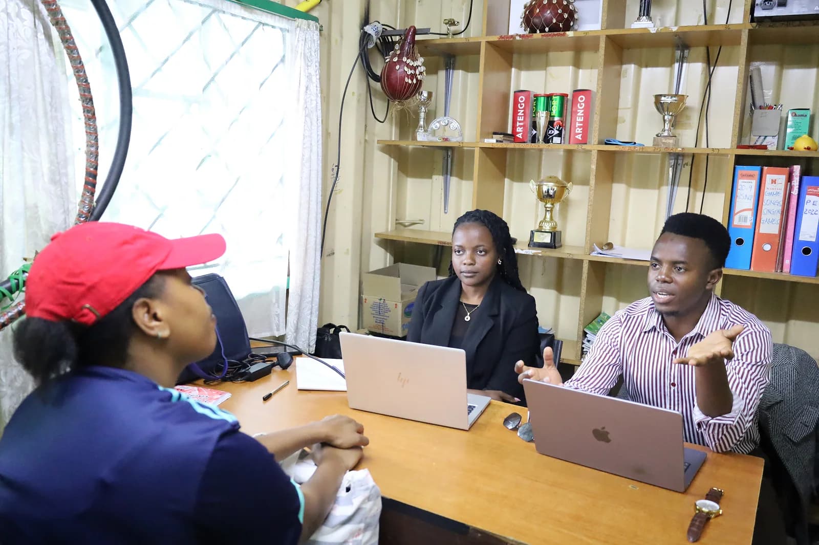 Two NairoBits team members with laptops talking with a visitor across a desk